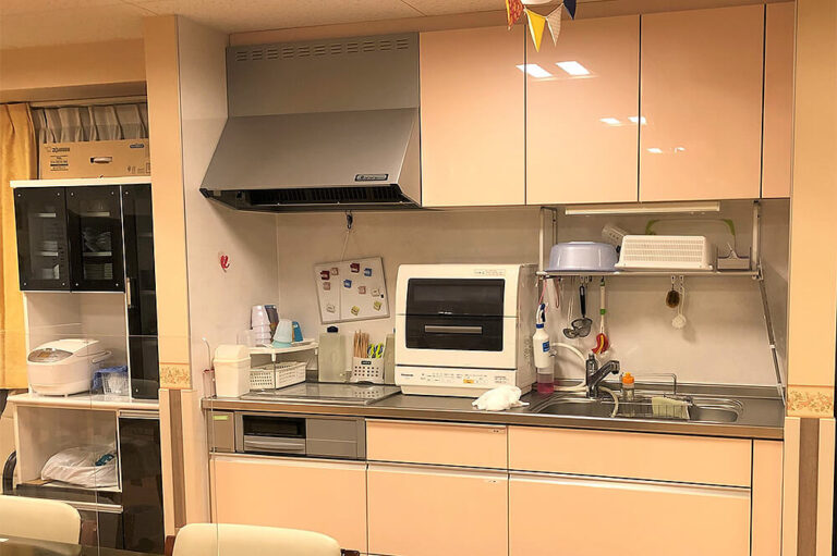 介護施設の共用キッチン。電子レンジ、炊飯器、食器棚が備わった調理スペース。